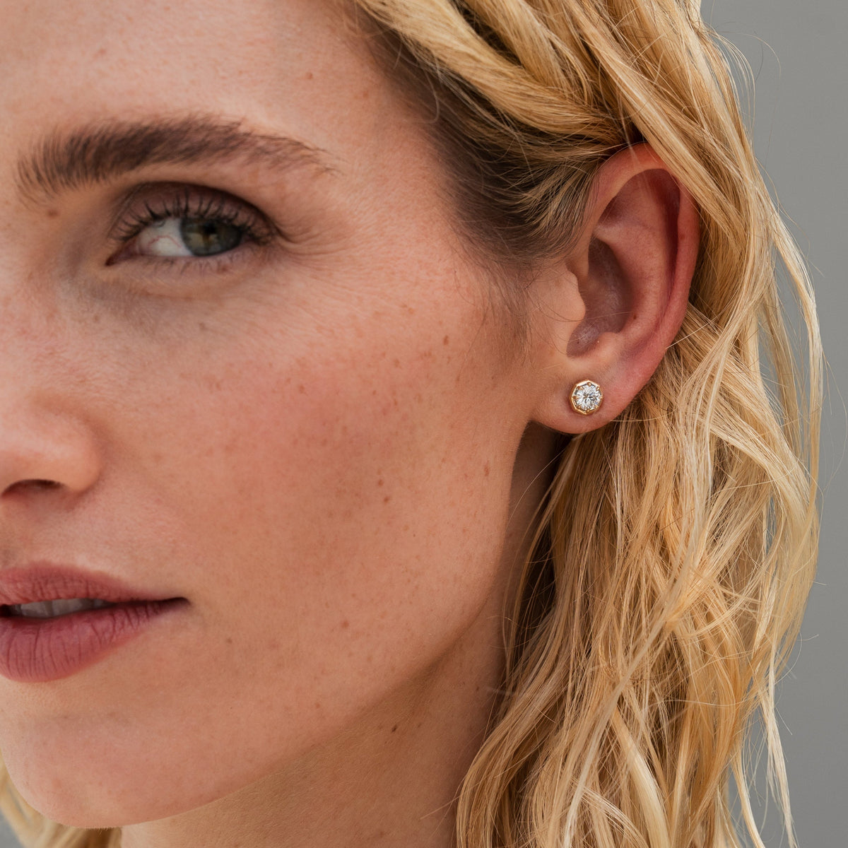 Close-up of a round gold stud earring with a round brilliant diamond and half bezel with octagonal shape with 8-prongs