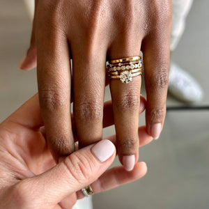 Model wearing 14k gold bezel set diamond ring stacked with an engagement ring