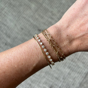 Model wearing 14k gold tennis bracelet with birdie-shaped links with diamonds stacked with other gold bracelets