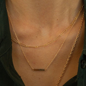 Model wearing 14k gold engravable nameplate necklace stacked with other necklaces