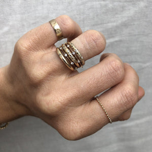 Model wearing a thin 14k gold ring with diamonds stacked with several other gold rings