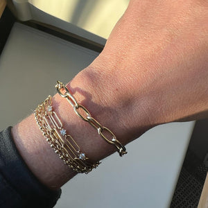 Model wearing 14k gold charm bracelet stacked with other bracelets